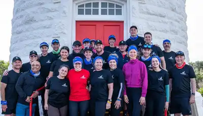 "Group photo of team members gathered outside a white lighthouse with a red door, representing Scott Bader's community initiatives." [G]