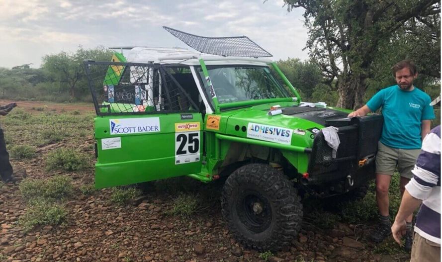 "Green off-road rally vehicle #25 featuring Scott Bader adhesives branding, with team members in outdoor terrain setting" [G]