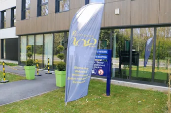 "Modern office building entrance with Scott Bader banner flag displaying company information and directional signage" [G]