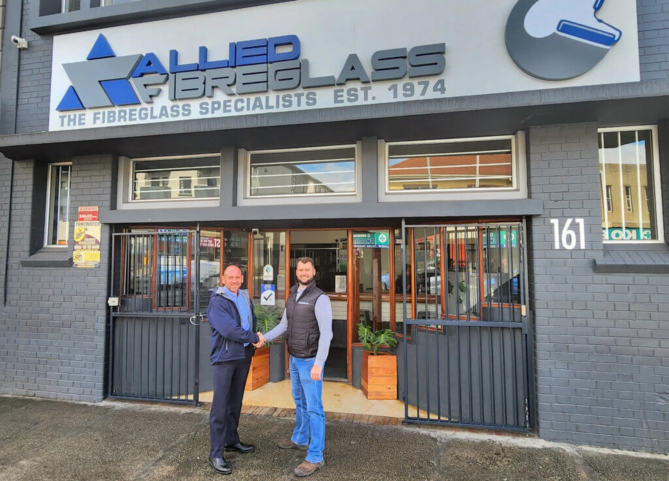 "Allied Fibreglass storefront with two professionals shaking hands, specialists in composites and resins since 1974" [G]