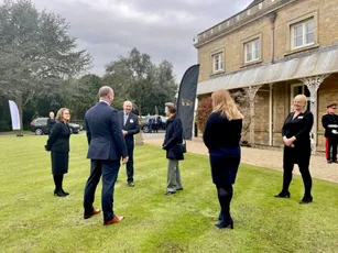 "Scott Bader business gathering on the lawn of a historic stone building with attendees networking under cloudy skies" [G]