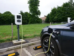 Electric vehicle charging station with car plugged in at a green countryside location. [G]