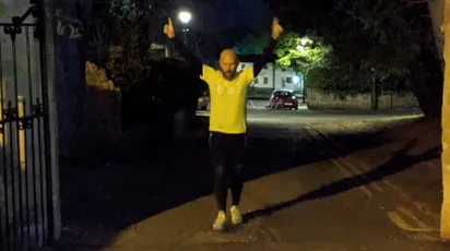 Person in bright yellow top standing on a nighttime street with arms outstretched [G]