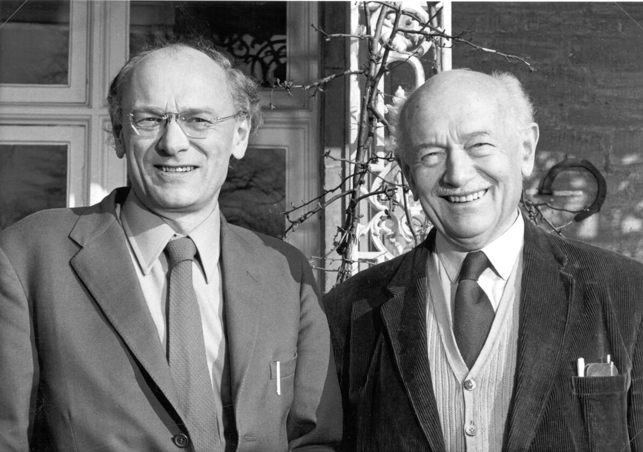 "Historic black and white photograph of two smiling businessmen outside a building, representing Scott Bader's leadership in composites and resins" [G]