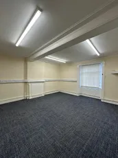 Empty office room with blue carpet, cream walls, and fluorescent lighting. [G]