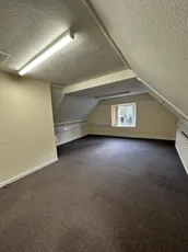 Empty attic room with sloped ceiling, carpet flooring, and a single window. [G]