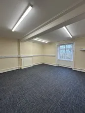 Empty office room with carpet flooring and large window, no branding visible in the image. [G]