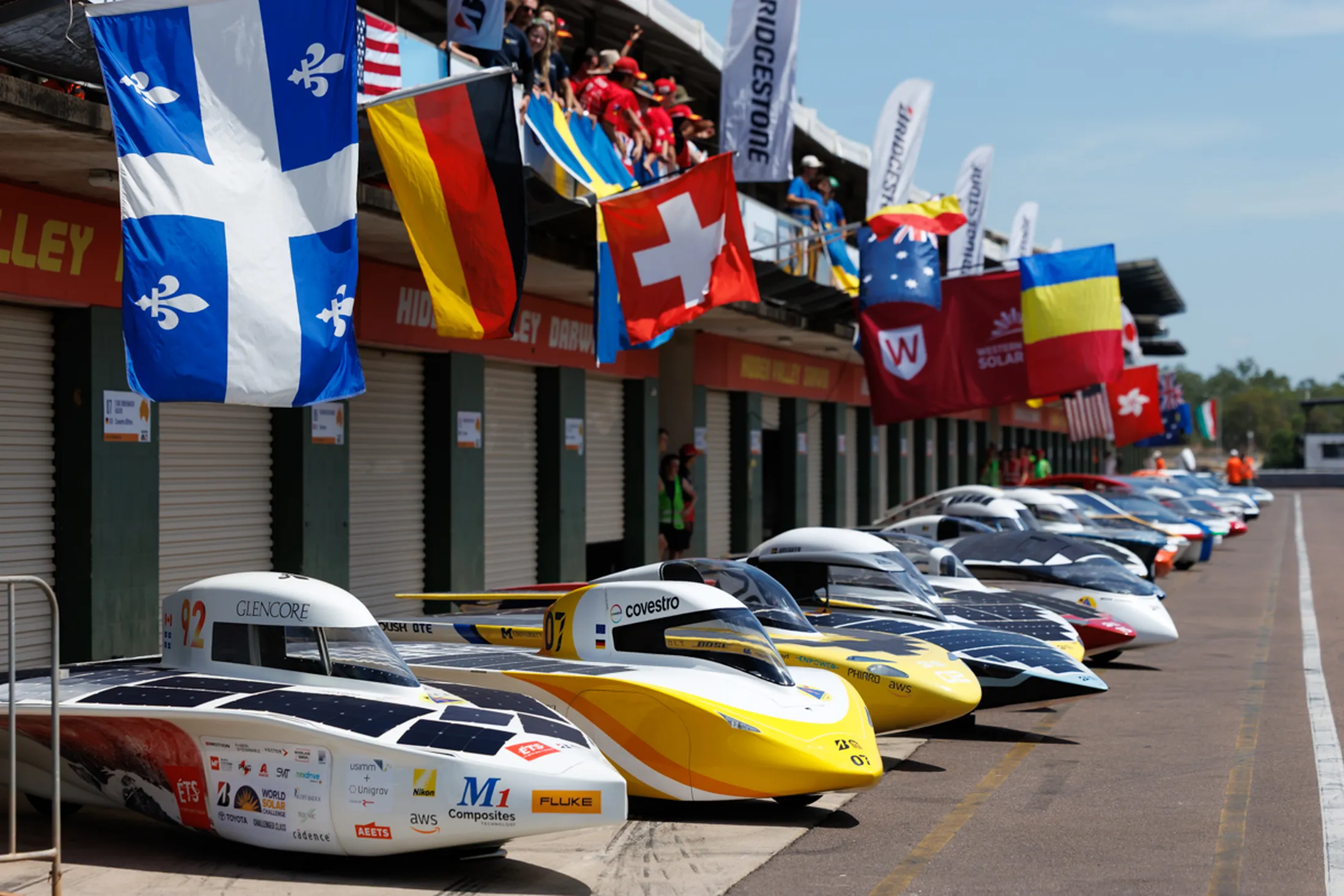 Solar race cars lined up at track pit lane, built with Scott Bader composites and resins for lightweight performance. [G]