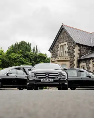 "Three luxury Mercedes-Benz vehicles parked in front of a stone building with cloudy sky backdrop." [G]