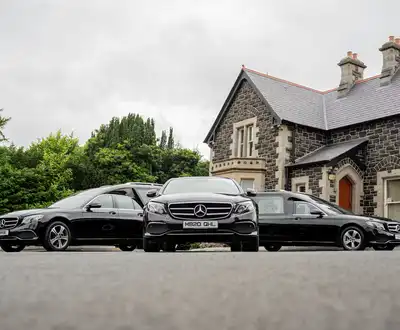 "Three luxury Mercedes-Benz vehicles parked in front of a stone building with cloudy sky backdrop." [G]