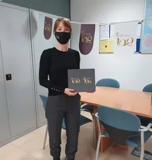 "Person in office holding branded materials with decorative banners in background celebrating 100 years milestone" [G]