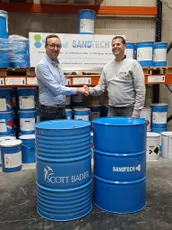 Two men shaking hands beside Scott Bader drums, celebrating a partnership supplying resins and gelcoats to Sandtech. [G]