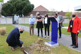 "Group of masked professionals gathered around a blue podium installation during an outdoor ceremony at Scott Bader facility" [G]