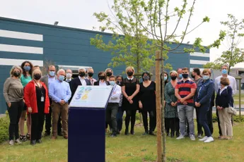 "Group gathered outside Scott Bader facility for presentation event, with modern building and newly planted tree in foreground" [G]