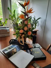 "Elegant floral arrangement with bird of paradise flowers and roses on office desk with Scott Bader promotional materials" [G]