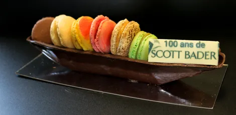 "Colorful macarons on a chocolate display celebrating '100 ans de Scott Bader' anniversary" [G]