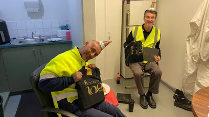 "Two workers in high-visibility safety vests taking a break in a facility break room at Scott Bader, specialists in composites and adhesives." [G]