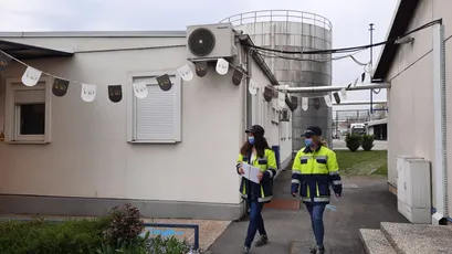 "Industrial facility with storage tank and workers in safety gear at Scott Bader manufacturing site for resins and composites" [G]