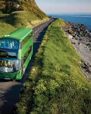 "Green double-decker bus traveling along coastal road with ocean view, showcasing Scott Bader composites in transportation applications" [G]