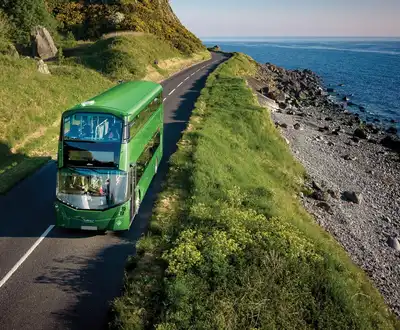 "Green double-decker bus traveling along coastal road with ocean view, showcasing Scott Bader composites in transportation applications" [G]