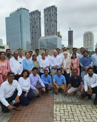 "Group photo of Scott Bader team members gathered at an outdoor urban location with modern skyscrapers in the background" [G]