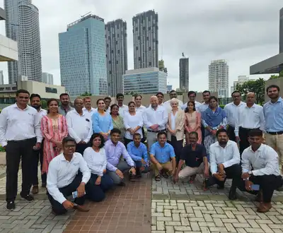 "Group photo of Scott Bader team members gathered at an outdoor urban location with modern skyscrapers in the background" [G]