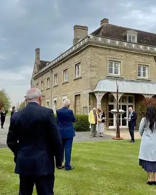 "Scott Bader corporate event at historic stone building with attendees gathered on manicured lawn under cloudy sky" [G]