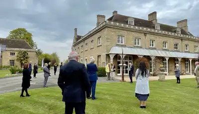"Scott Bader corporate event at historic stone building with attendees gathered on manicured lawn under cloudy sky" [G]