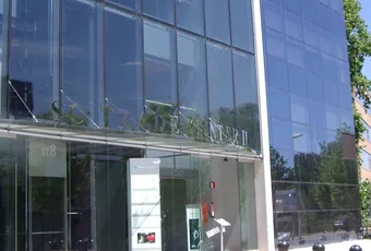 "Modern glass office building exterior with reflective facade, surrounded by trees in an urban business setting" [G]
