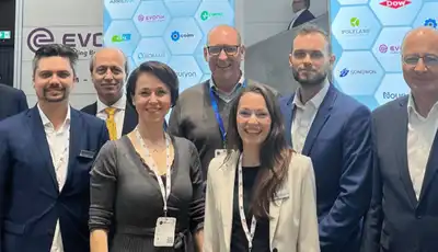 "Group of professionals at industry event with Scott Bader branding visible on hexagonal backdrop display" [G]