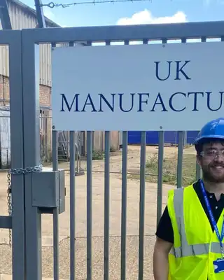 "Scott Bader UK manufacturing facility entrance with safety-equipped worker in high-visibility vest and hard hat" [G]