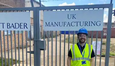 "Scott Bader UK manufacturing facility entrance with safety-equipped worker in high-visibility vest and hard hat" [G]