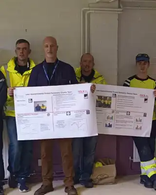 "Group of professionals in safety vests displaying informational posters in an industrial setting, representing Scott Bader's commitment to technical training." [G]