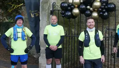 "Group of runners in bright yellow safety shirts gathered at a stone entrance with decorative balloons, representing Scott Bader community event" [G]