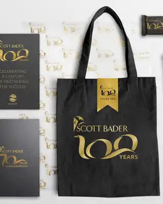 "Scott Bader 100 years commemorative merchandise collection featuring branded tote bag, notebook, travel mug and promotional materials" [G]