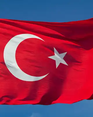 "Turkish flag with red background and white crescent moon and star waving against blue sky" [G]