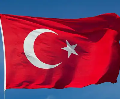 "Turkish flag with red background and white crescent moon and star waving against blue sky" [G]