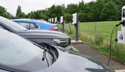 "Electric vehicle charging station with multiple cars parked in a green countryside setting" [G]