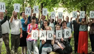 "Group holding 'THANK YOU SCOTT BADER' letter cards in outdoor setting, celebrating the company's composites and adhesives" [G]