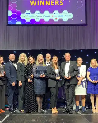 "Award winners on stage at industry event with Scott Bader representatives holding trophies against purple-lit backdrop" [G]