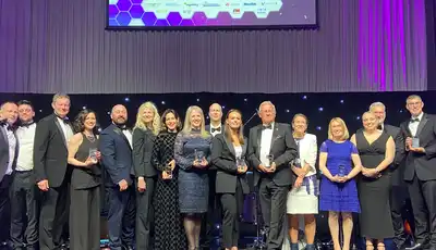 "Award winners on stage at industry event with Scott Bader representatives holding trophies against purple-lit backdrop" [G]