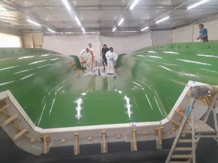 Workers applying Scott Bader gelcoats and resins to a large green composite boat hull mold. [G]