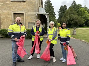 "Team in high-visibility vests participating in community cleanup outside historic stone building with Scott Bader support" [G]
