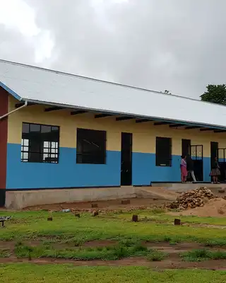 "Rural school building with blue walls and metal roof, featuring water storage tanks on the left side under cloudy sky" [G]