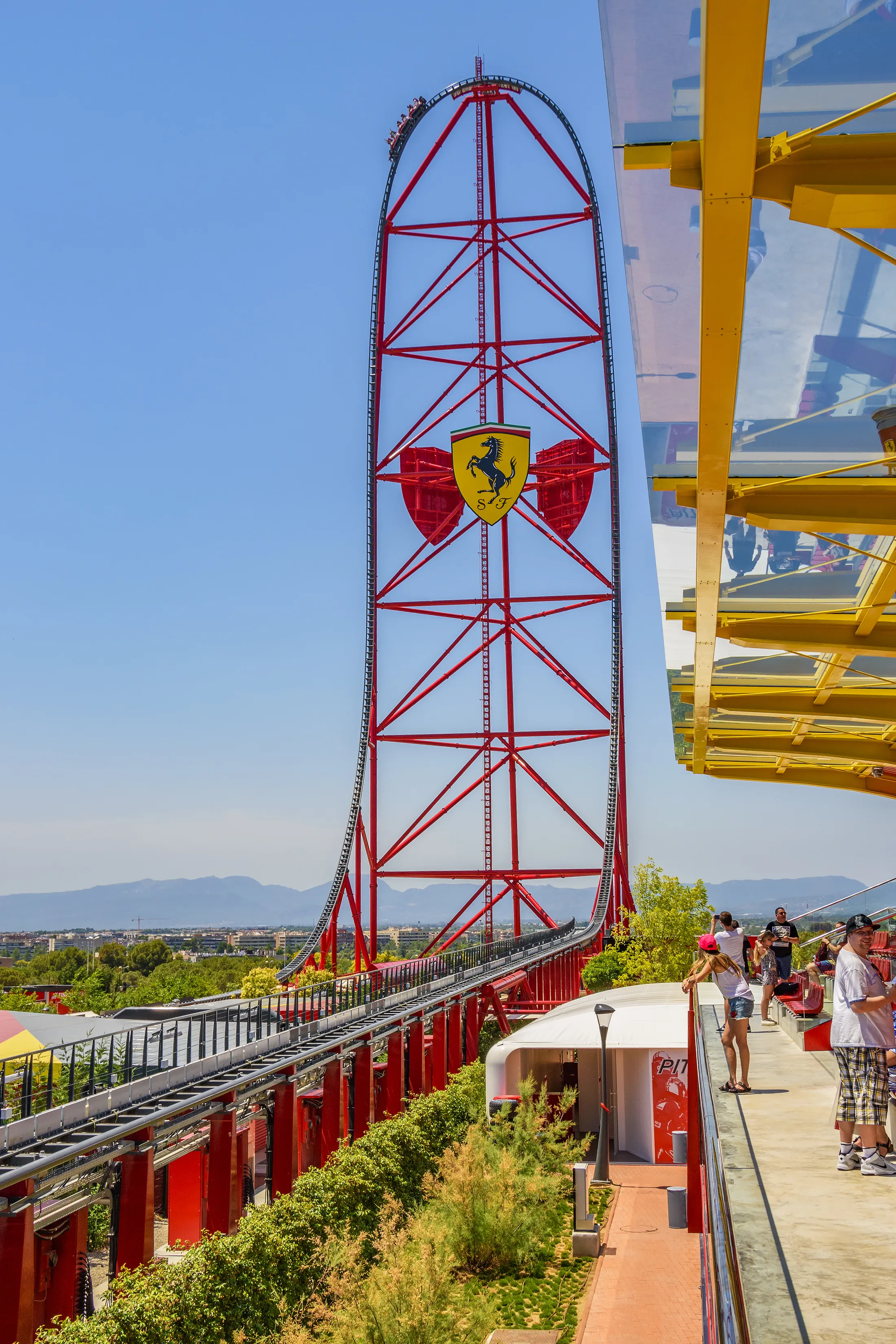 "Red Accelerator roller coaster with Ferrari logo at theme park against blue sky, showcasing structural engineering." [G]