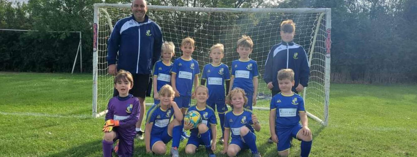 "Youth football team in blue uniforms posing on green field with soccer goal in background" [G]