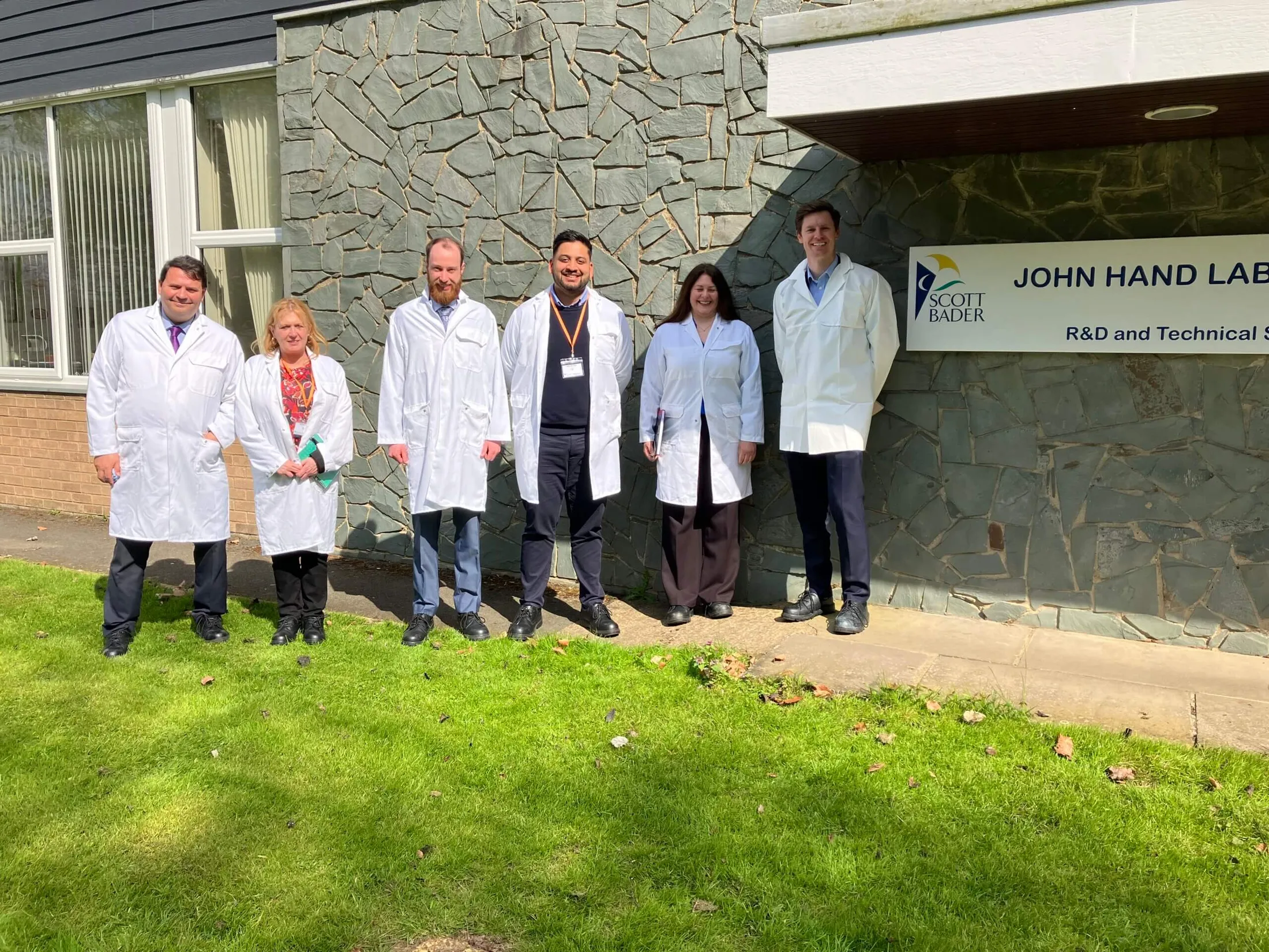 "Team of laboratory professionals in white coats outside the John Hand Lab R&D facility where Scott Bader develops advanced resins and composites" [G]