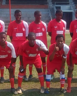"Soccer team in red uniforms posing on field with stadium seating in background" [G]