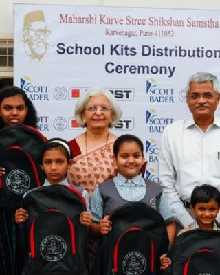 "School kits distribution ceremony with children holding backpacks, sponsored by Scott Bader and other organizations supporting education initiatives." [G]