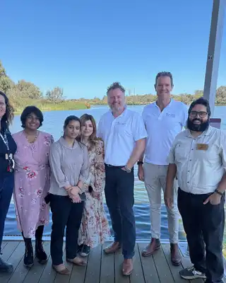 "Group gathered on wooden dock overlooking water on sunny day with clear blue sky" [G]